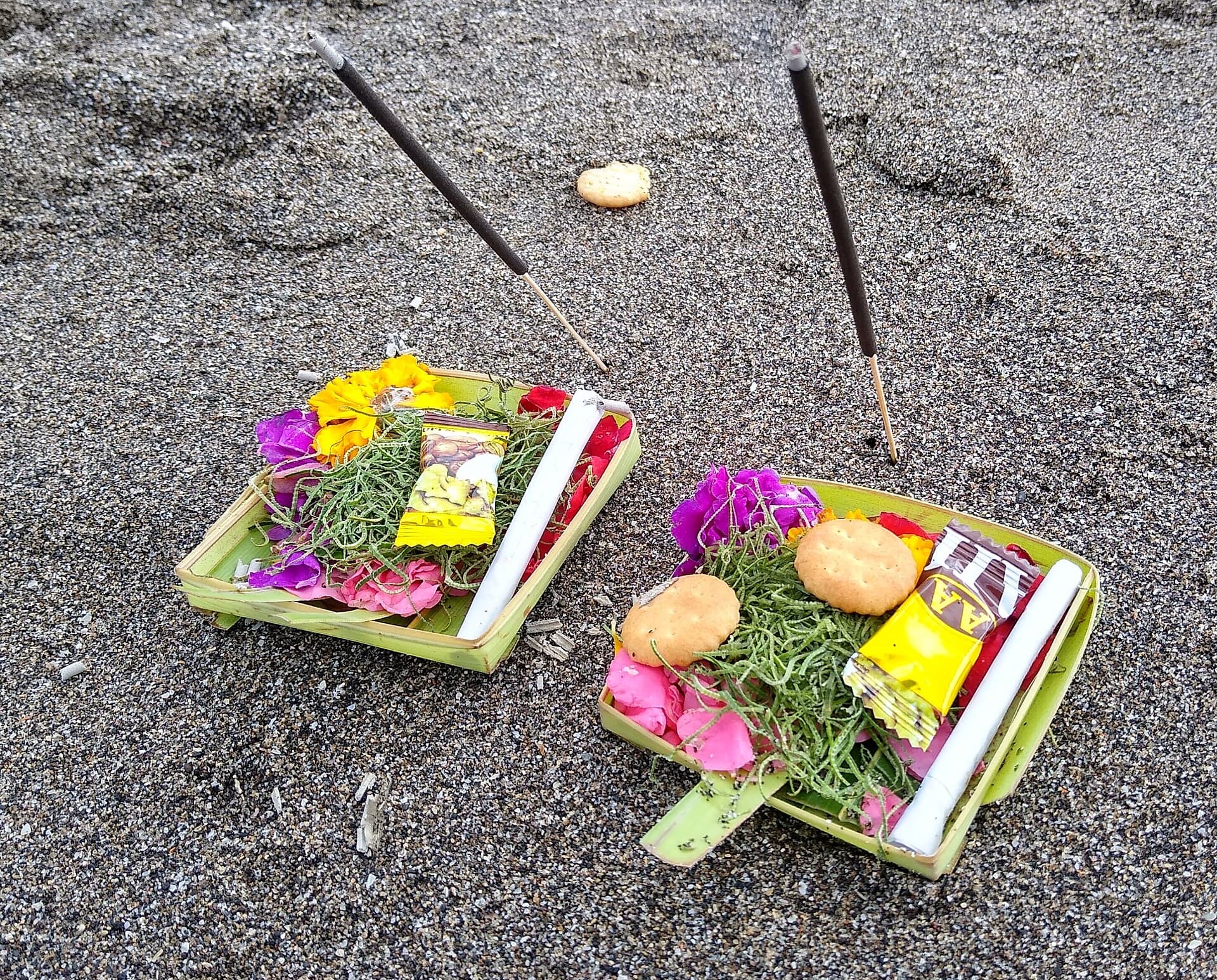 Twee canang sari-offers met bloemen op zwart zand