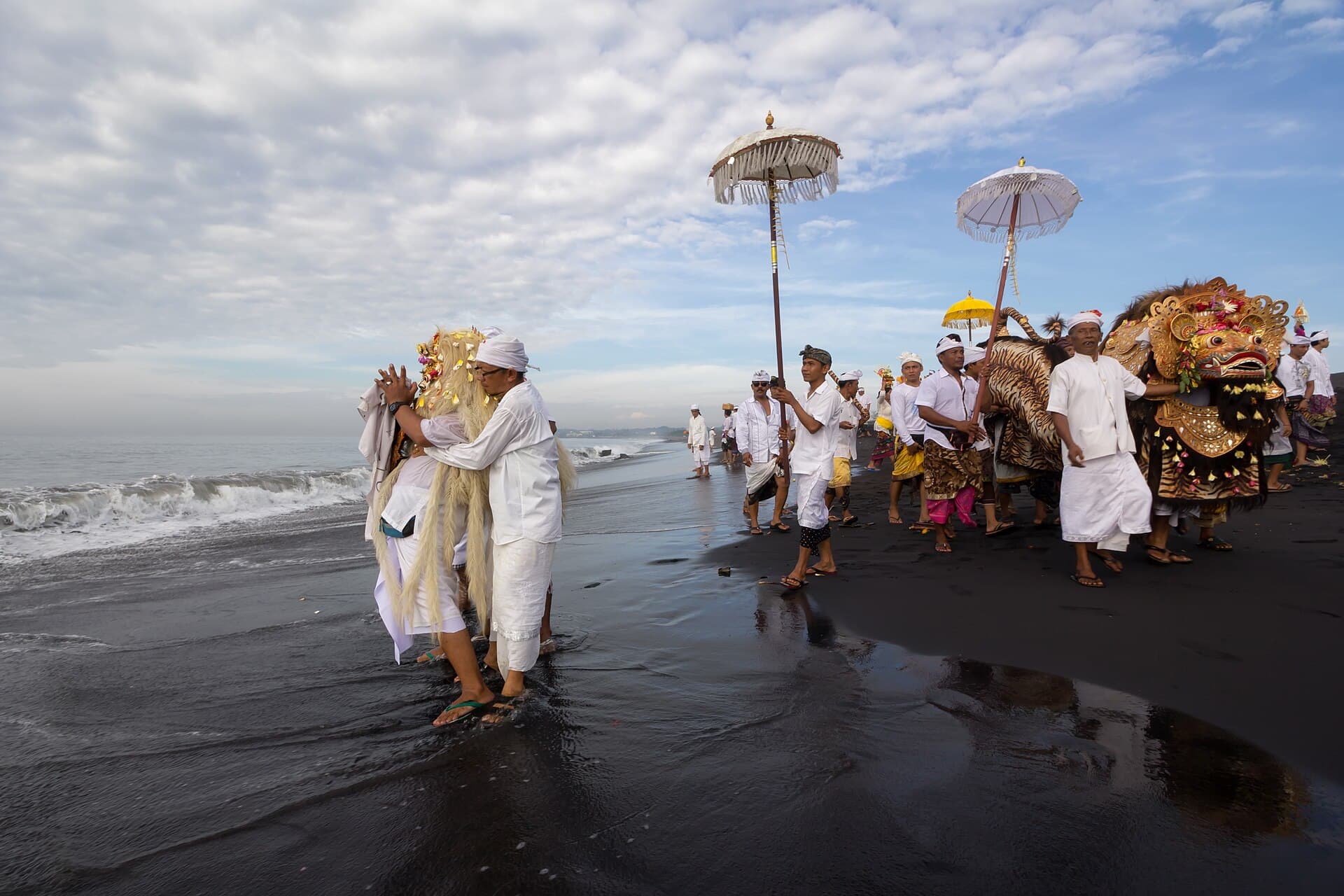 Melasti-ceremonie op het strand met een Barong-figuur en gelovigen in het wit